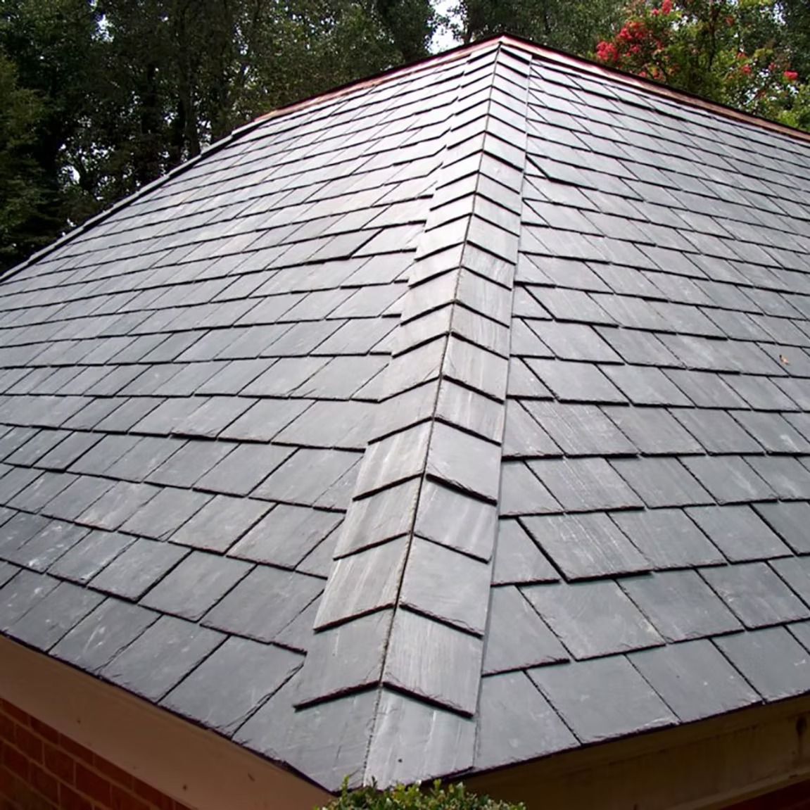 Gray shingle hip roof with a central ridge, viewed from below against trees