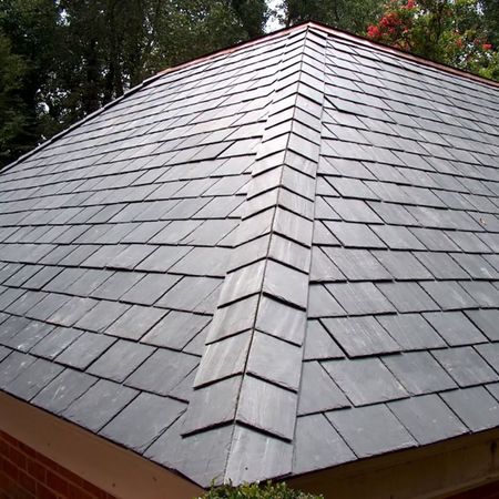 Gray shingle hip roof with a central ridge, viewed from below against trees