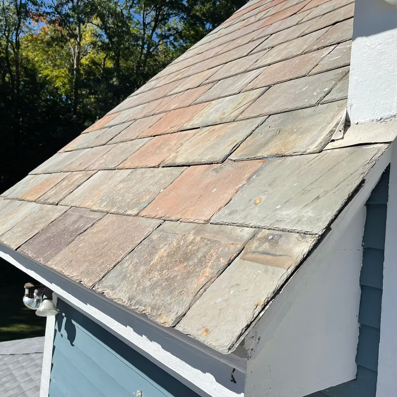 Sloped slate roof on a blue house with white trim, viewed from the side.