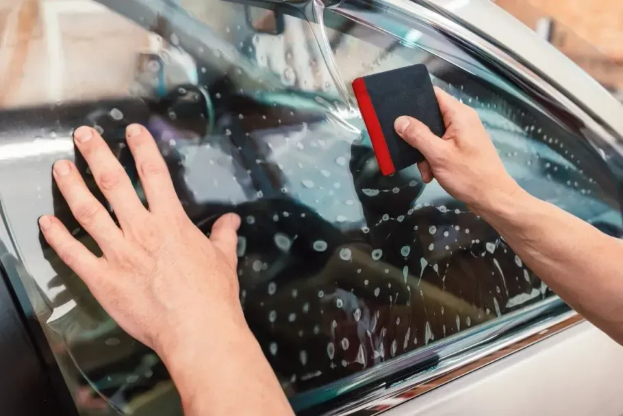 Using a squeegee to smooth ceramic tint on a vehicle window.