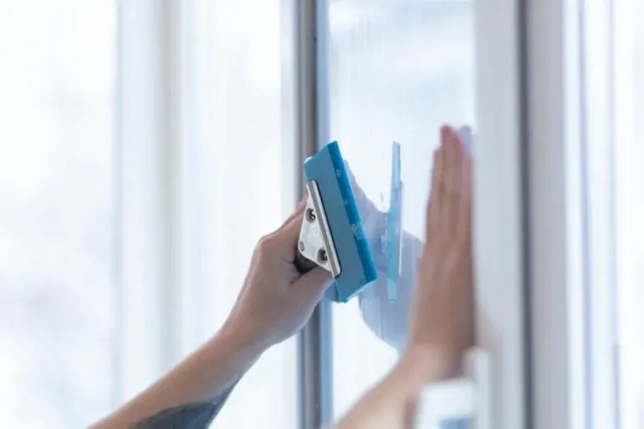 Close-up of a blue squeegee smoothing film on residential glass