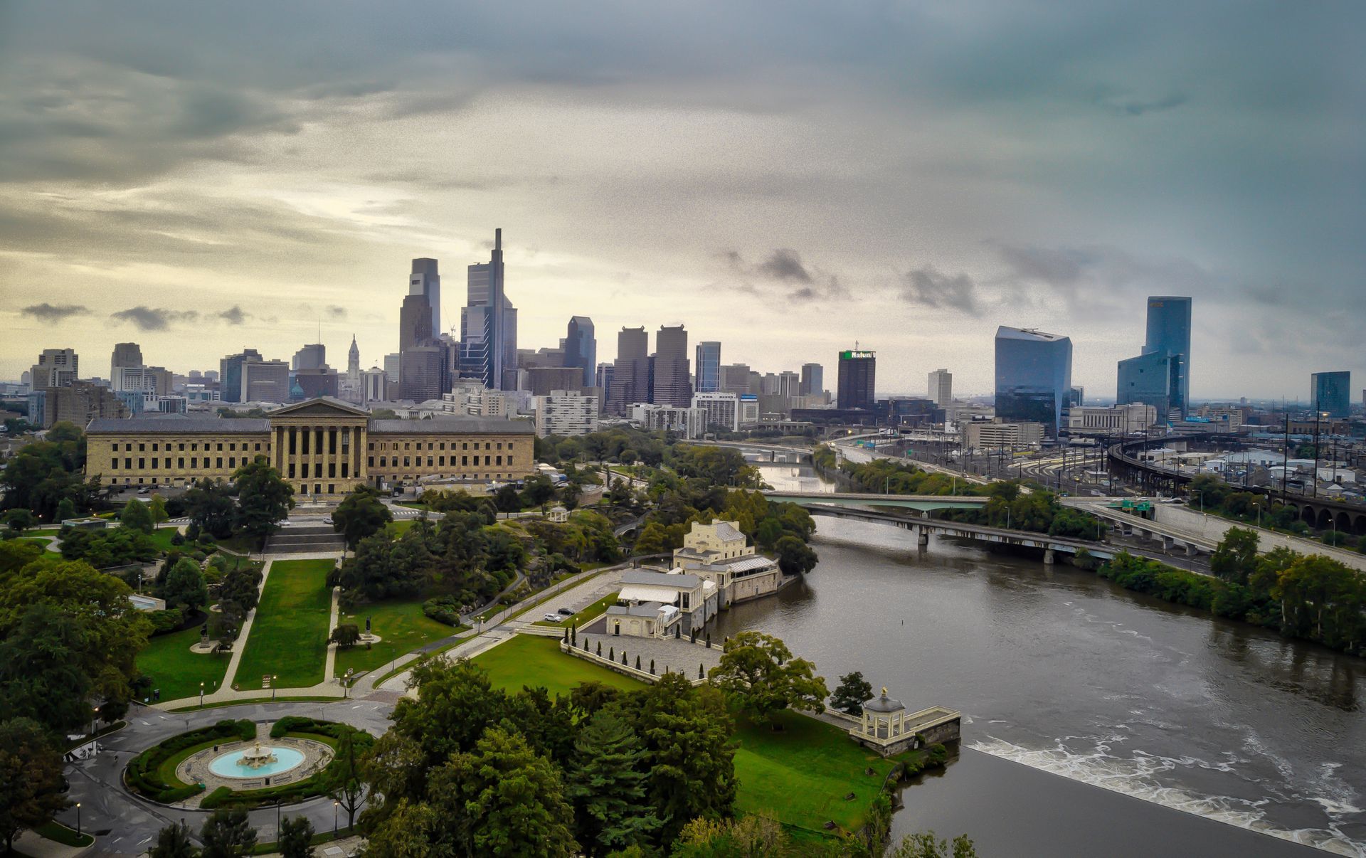 City skyline with river and park at dusk, featuring tall buildings and a bridge