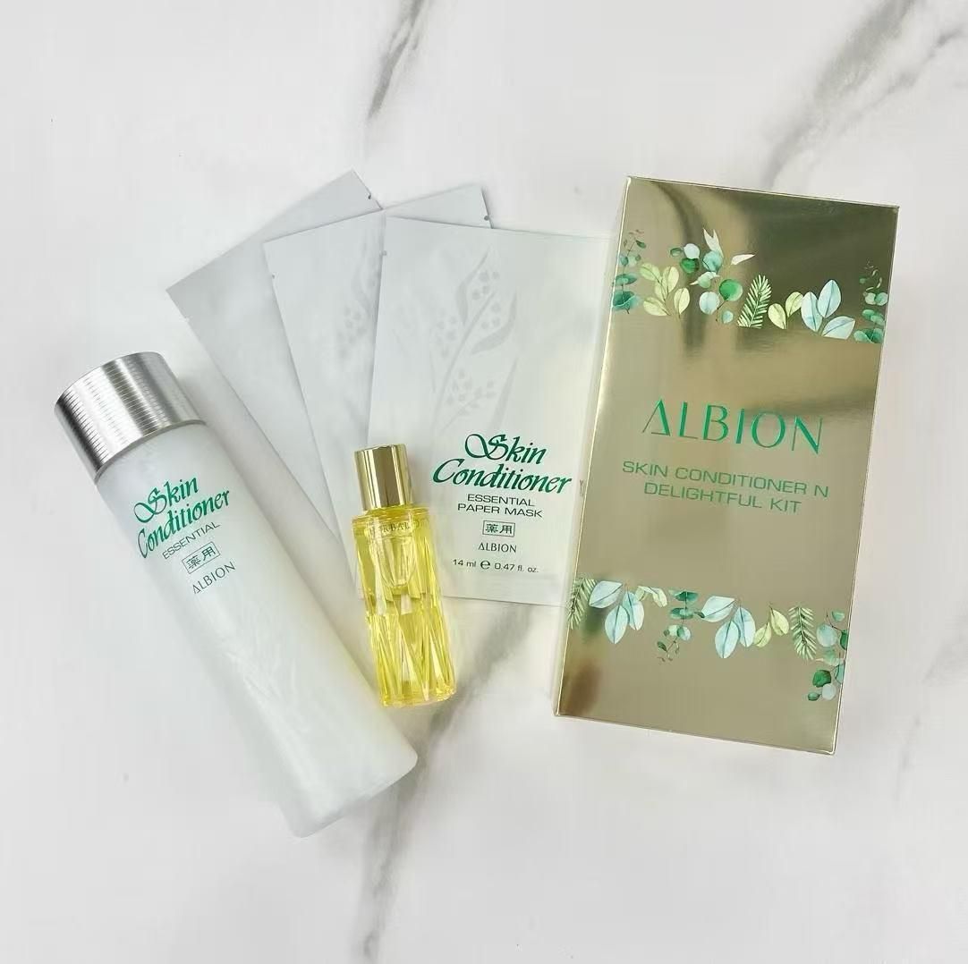 大理石表面上擺放著來自 Albion 的護膚產品：乳液、油、小包裝和帶有樹葉圖案的金色盒子。