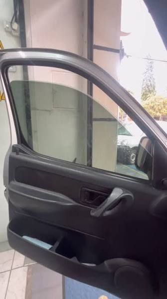 Puerta de coche abierta con interior negro, mostrando la ventana y el panel de la puerta junto a un edificio.