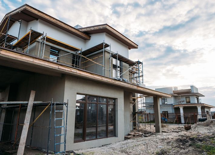 Modern two-story houses under construction with scaffolding on a muddy residential lot