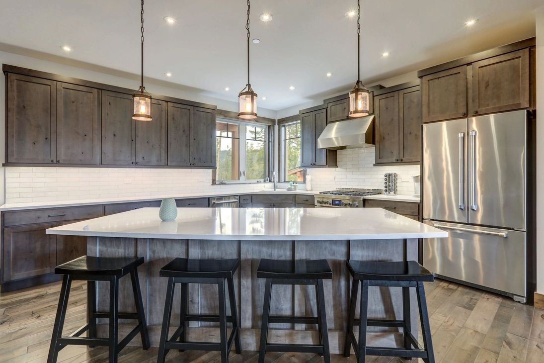 Modern kitchen with large island, pendant lights, wood cabinets, stainless steel fridge, and bar stools