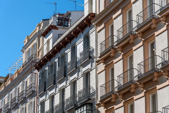 Row of ornate apartment balconies on a sunny street beneath a blue sky