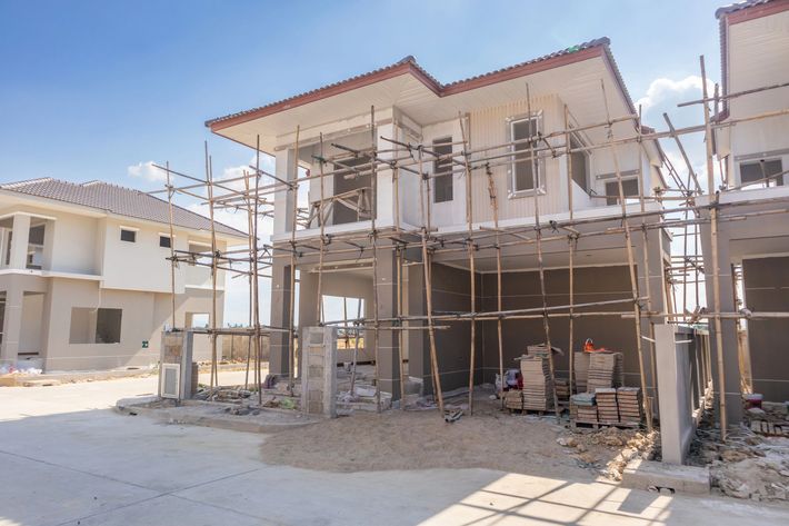 Two-story house under construction with scaffolding and building materials in a sunny residential area