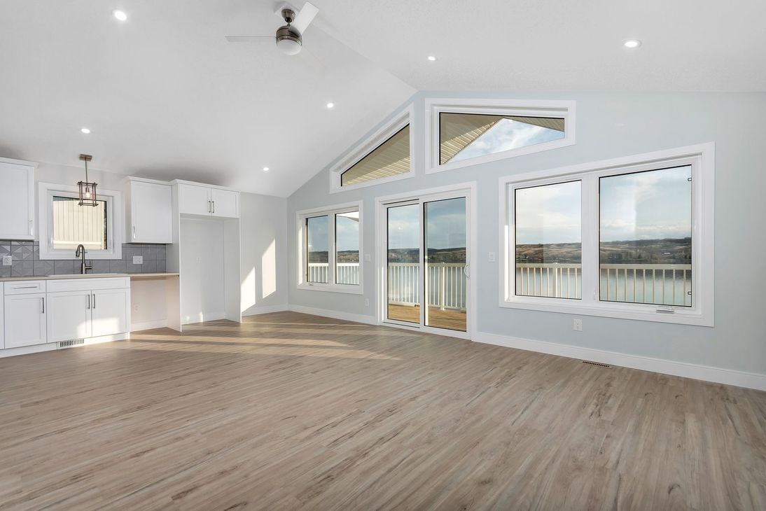 Bright empty open-plan living room with large windows, light wood floors, and a white kitchen area
