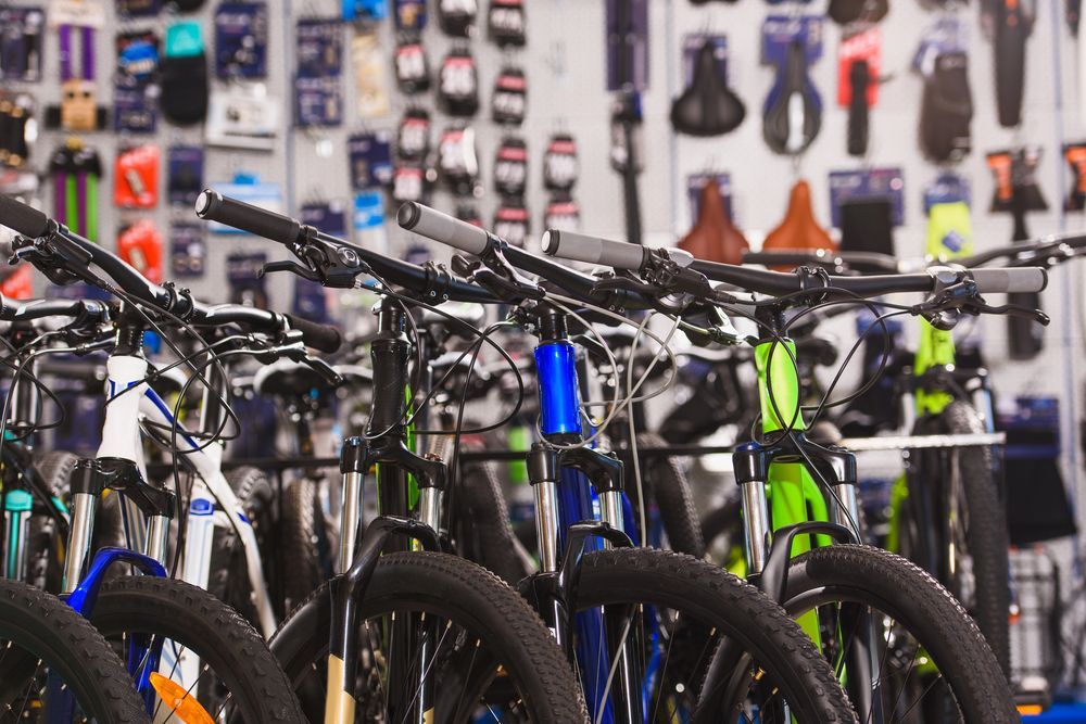 Biciclette in vendita in un negozio, con una varietà di colori e stili. Accessori visibili sulla parete sullo sfondo.