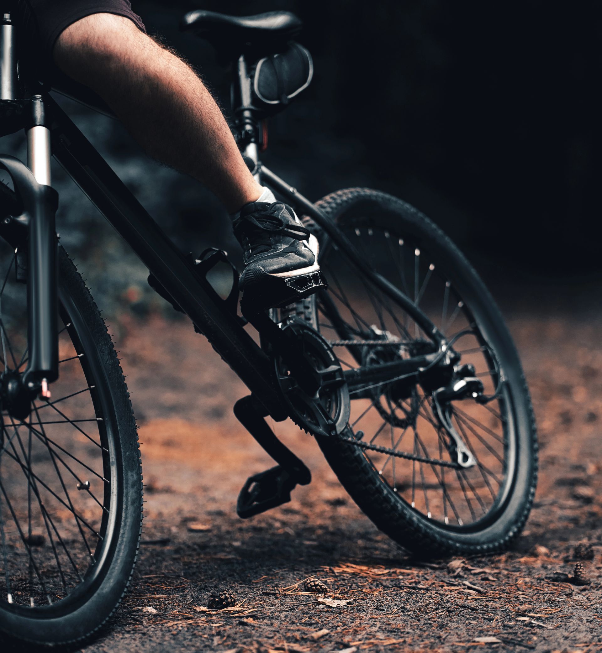 Piede di una persona sul pedale di una mountain bike nera su un sentiero sterrato in una foresta.