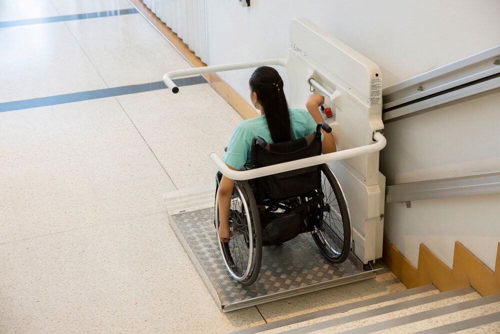 Woman in Wheelchair Using a Stair Lift on a Staircase — Peter Whelan Building Services in Wyoming, NSW