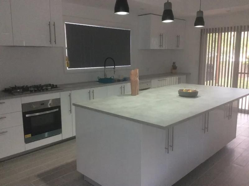 A Kitchen with White Cabinets and A Large Island — Peter Whelan Building Services in Wyoming, NSW