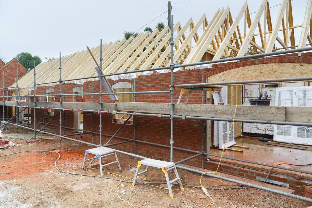 Brick Building With Scaffolding, Unfinished Roof Framing — Peter Whelan Building Services in Wyoming, NSW