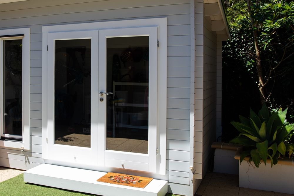 White Double Doors With Glass Panels on a Light Blue Wooden Building — Peter Whelan Building Services in Wyoming, NSW