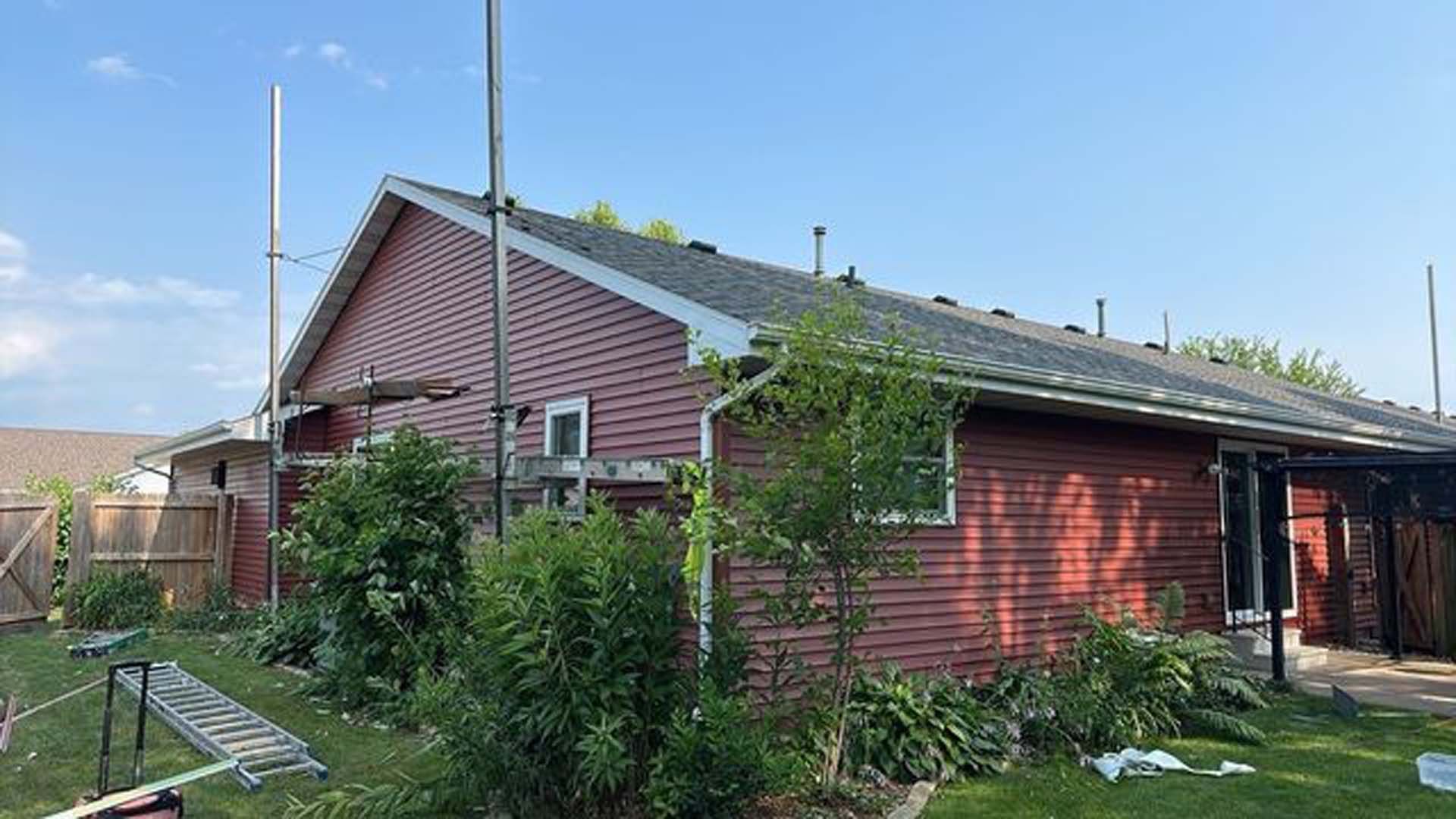 A red house with a gray roof is sitting in the middle of a lush green yard.