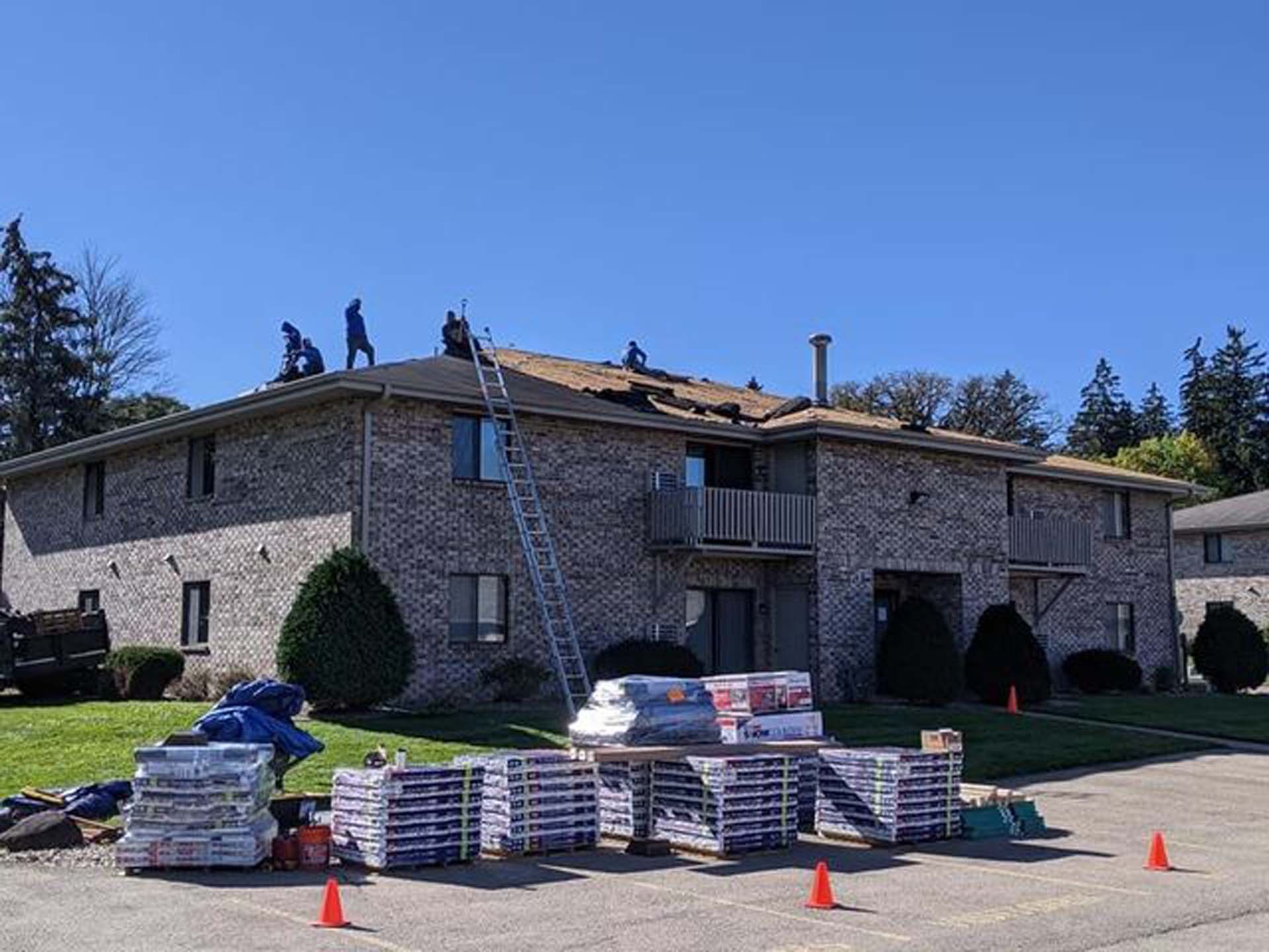 A group of people are working on the roof of a brick apartment building.