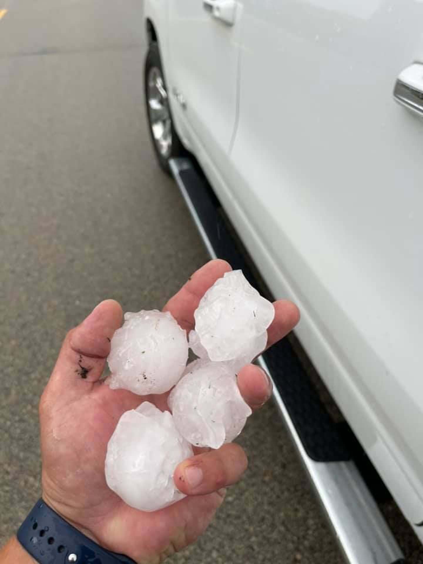 A person is holding hail in their hand in front of a white car.