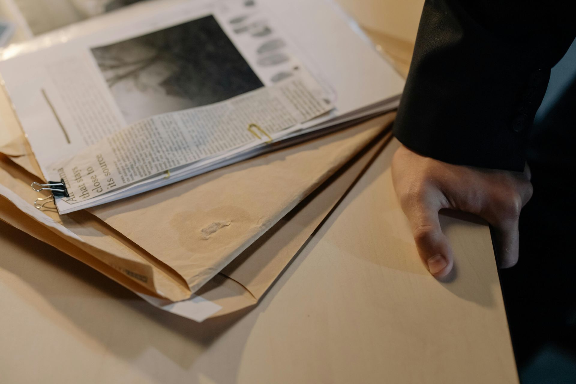 A person is holding a stack of envelopes and a newspaper on a table.