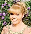A woman in a pink dress is smiling in front of purple flowers.