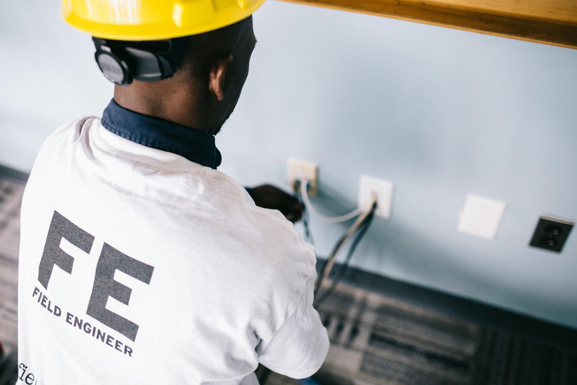 Field Engineer working on electrical outlets; wearing a yellow hard hat and white shirt.