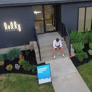 A person sits on the concrete steps of a modern cafe called Lolly, with a blue 