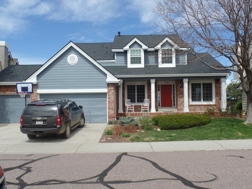 A two-story blue house with a red door, brick accents, a gray garage, and a car parked in the driveway.