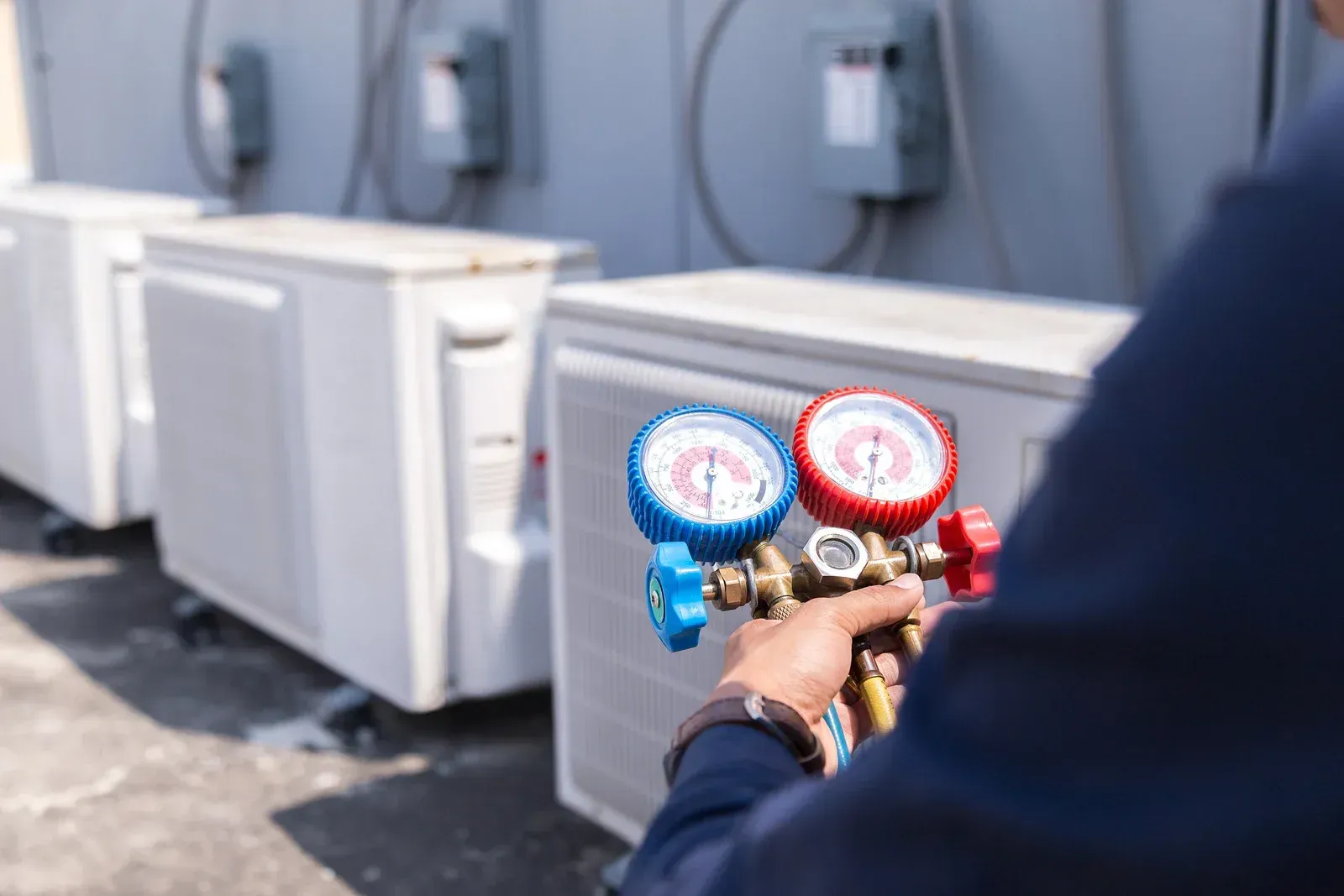 HVAC technician with gauges checking an outdoor AC unit, on a rooftop.