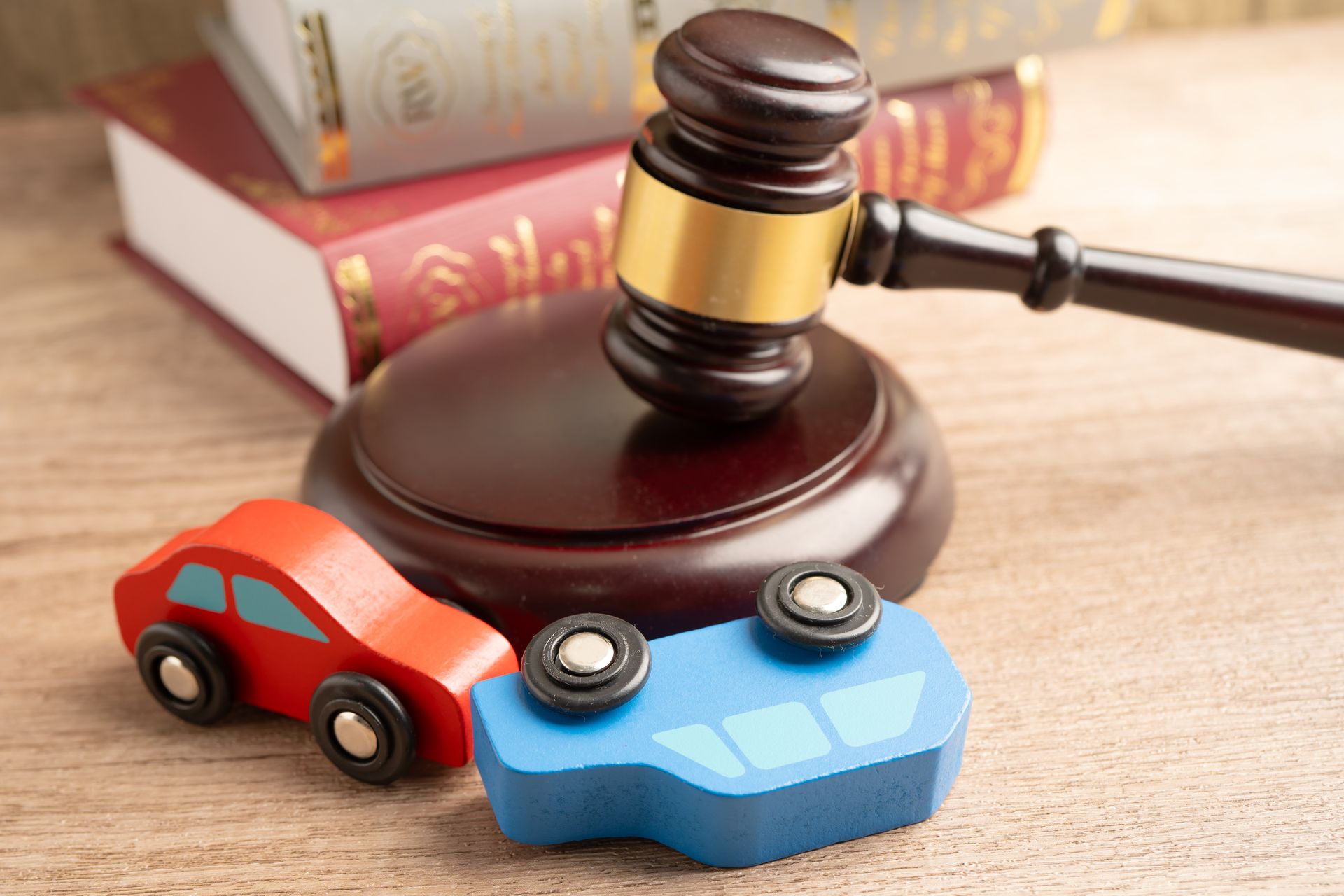 Wooden toy cars, one overturned, beside a judge’s gavel and law books, symbolizing car accident law. Wooden toy cars, one overturned, beside a judge’s gavel and law books, symbolizing car accident law.