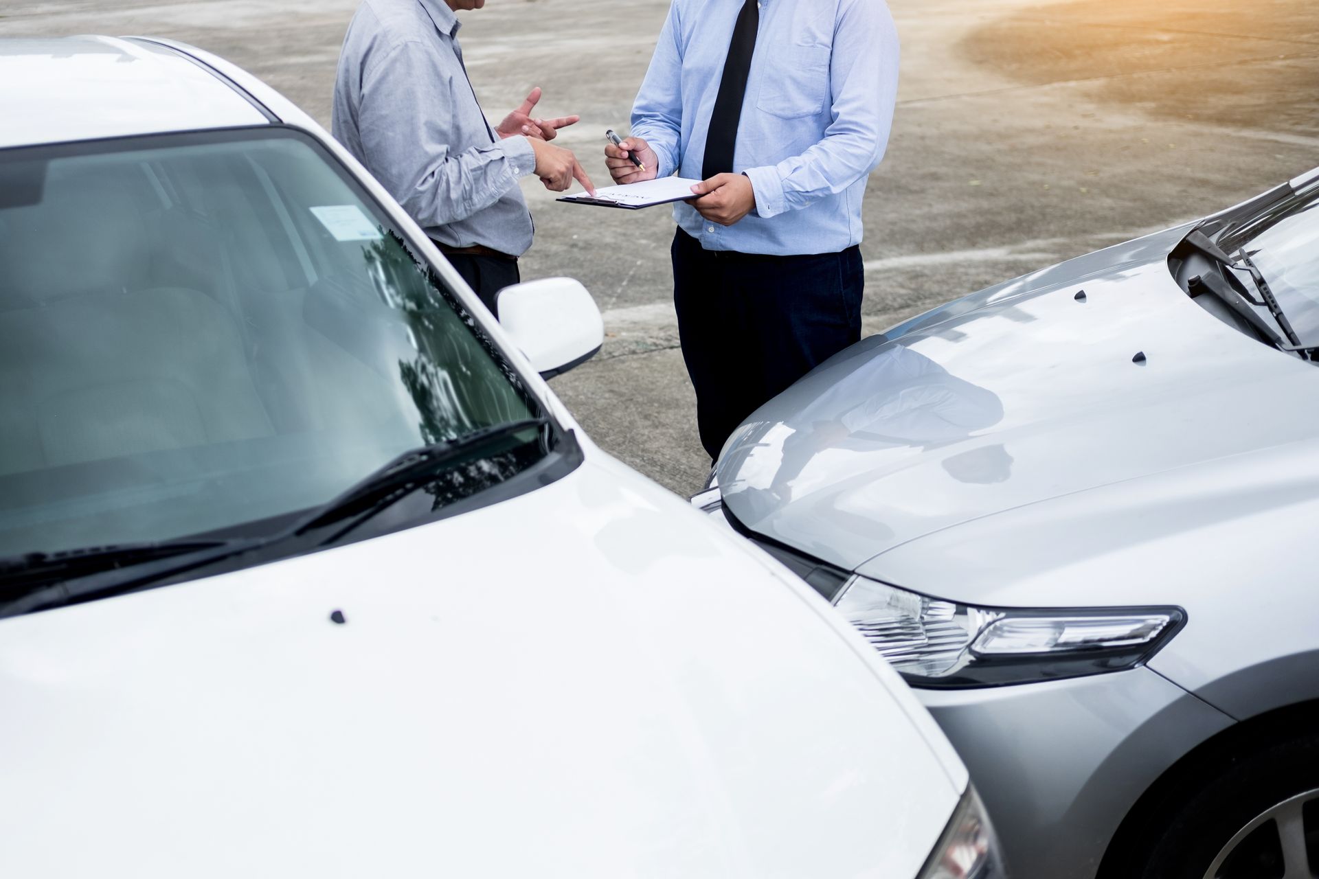 Two people inspect car damage and fill out paperwork after a minor collision.