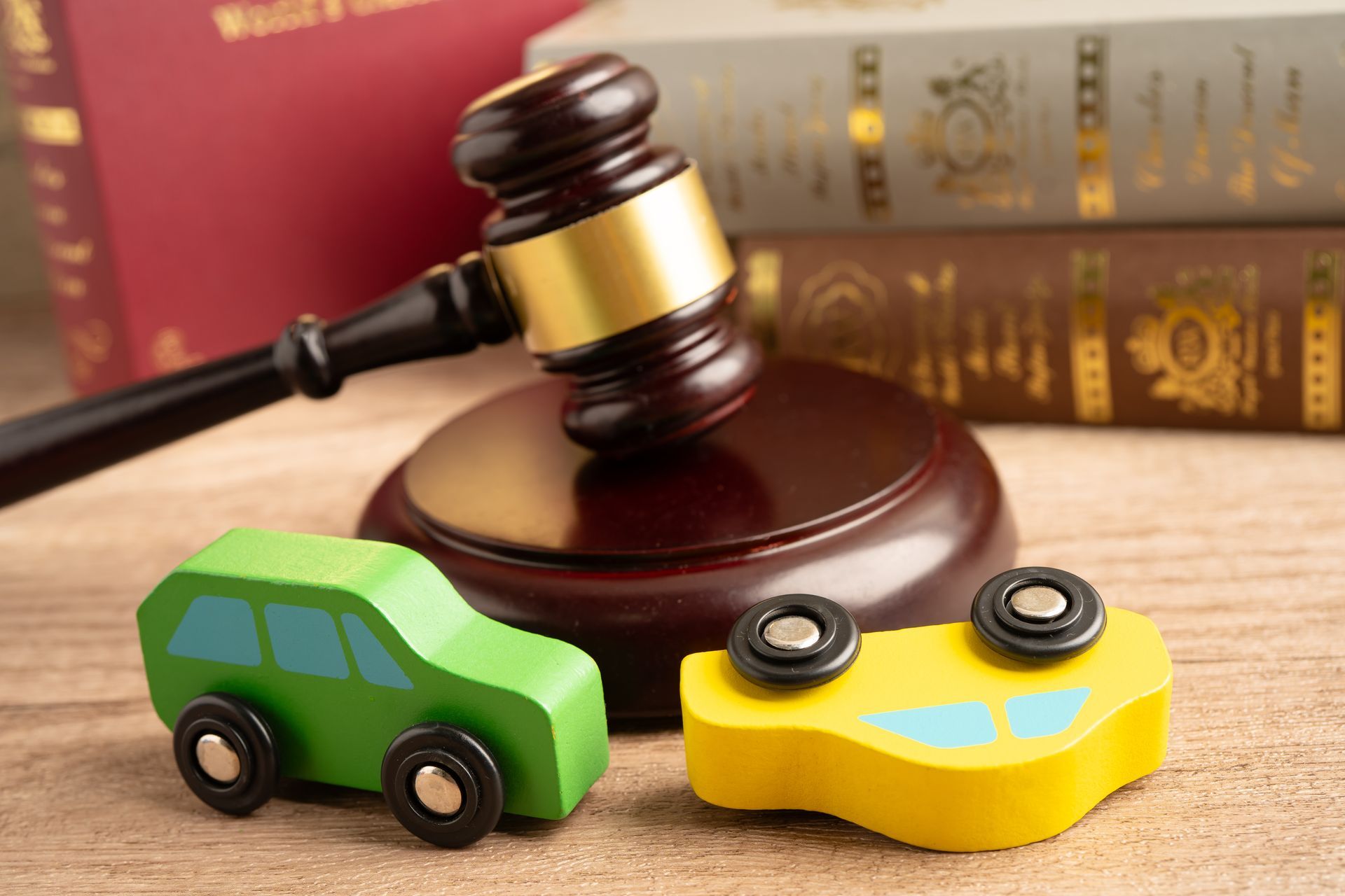 Toy cars and a gavel on a desk with law books in the background