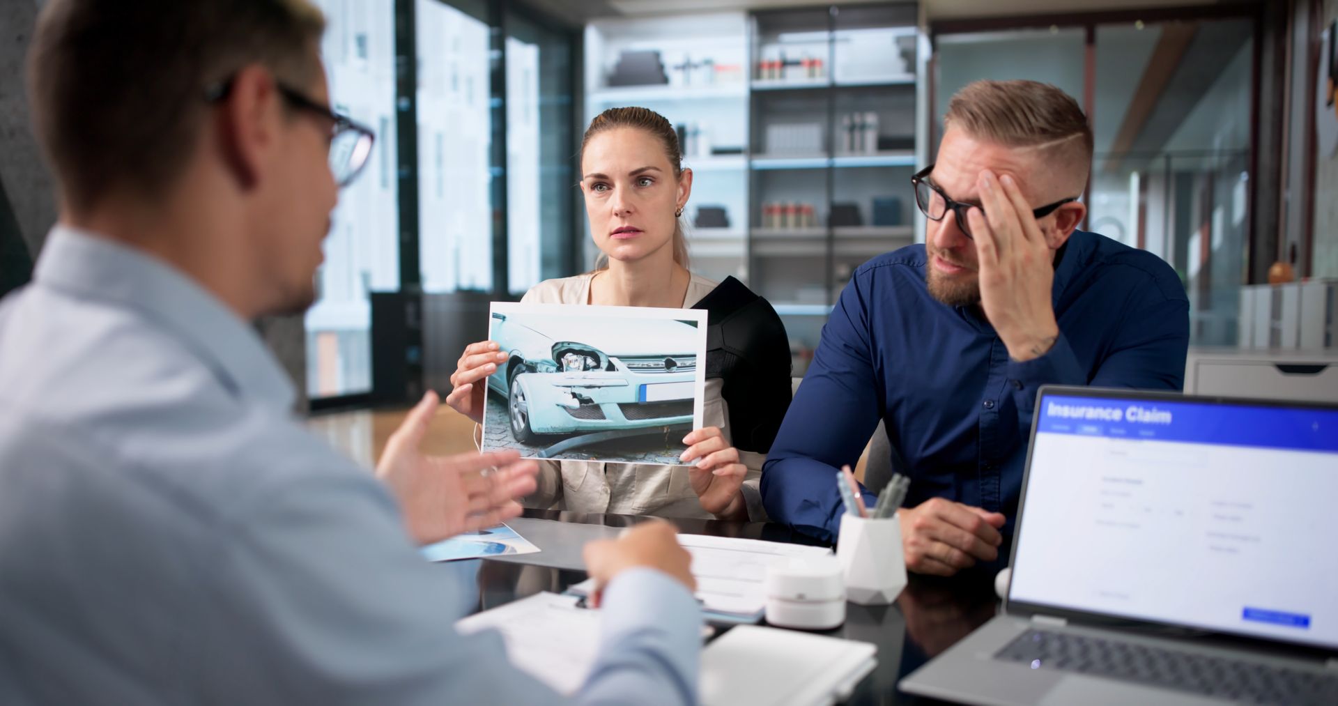 Professional car accident injury lawyer at desk with gavel, legal documents, and a model car. A car accident injury attorney reviews a case with a worried couple.