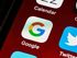 A close-up view of a smartphone home screen displaying the Google app icon among others on a red background.