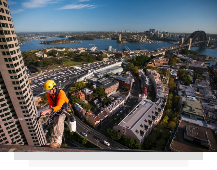 Worker rappels down a skyscraper, inspecting a window. Tablet displays a color-coded analysis chart.
