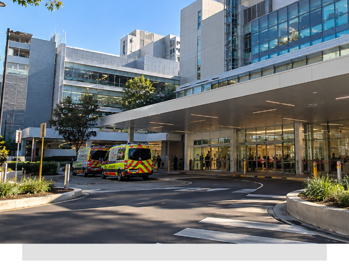 Ambulance parked under a hospital entrance canopy beside modern glass buildings