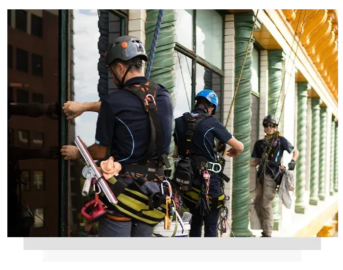 Window washers suspended on ropes cleaning a building's glass facade.