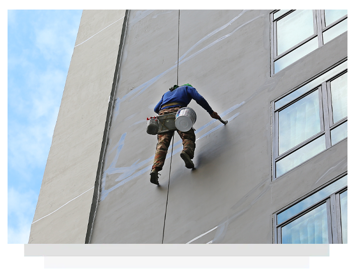Worker on ropes applying sealant to exterior wall of high-rise building.
