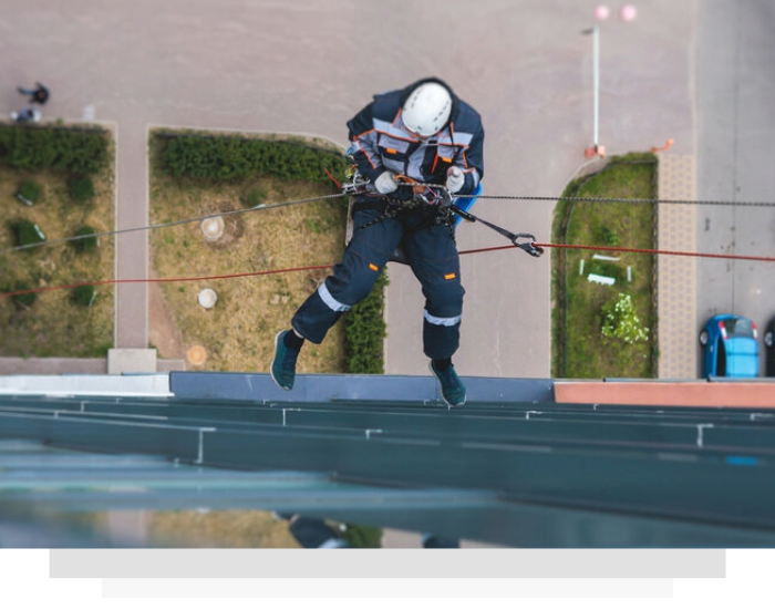 Rope technician in helmet and harness rappelling down a building wall beside rooftop planters