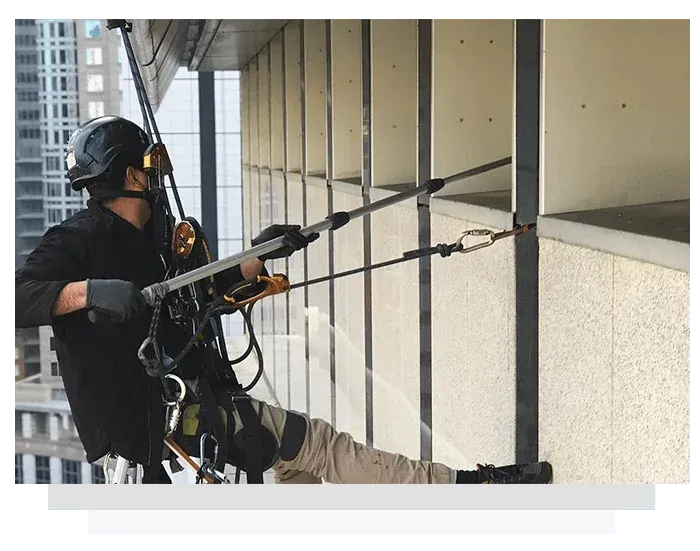 Rope access technician inspecting the exterior of a high-rise building, attached to ropes and using tools.