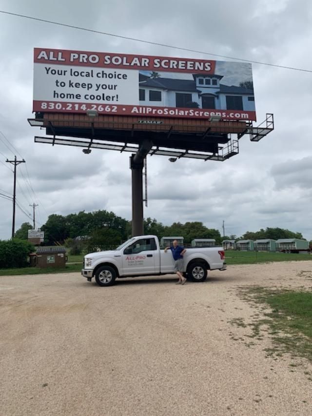 A white truck is parked in front of a billboard for all pro solar screens