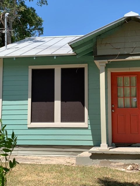 A green house with a red door and two windows