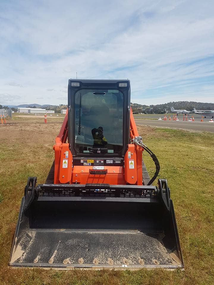 A Small Orange Bulldozer Is Parked In A Grassy Field — Grants Excavations In Osbornes Flat, VIC