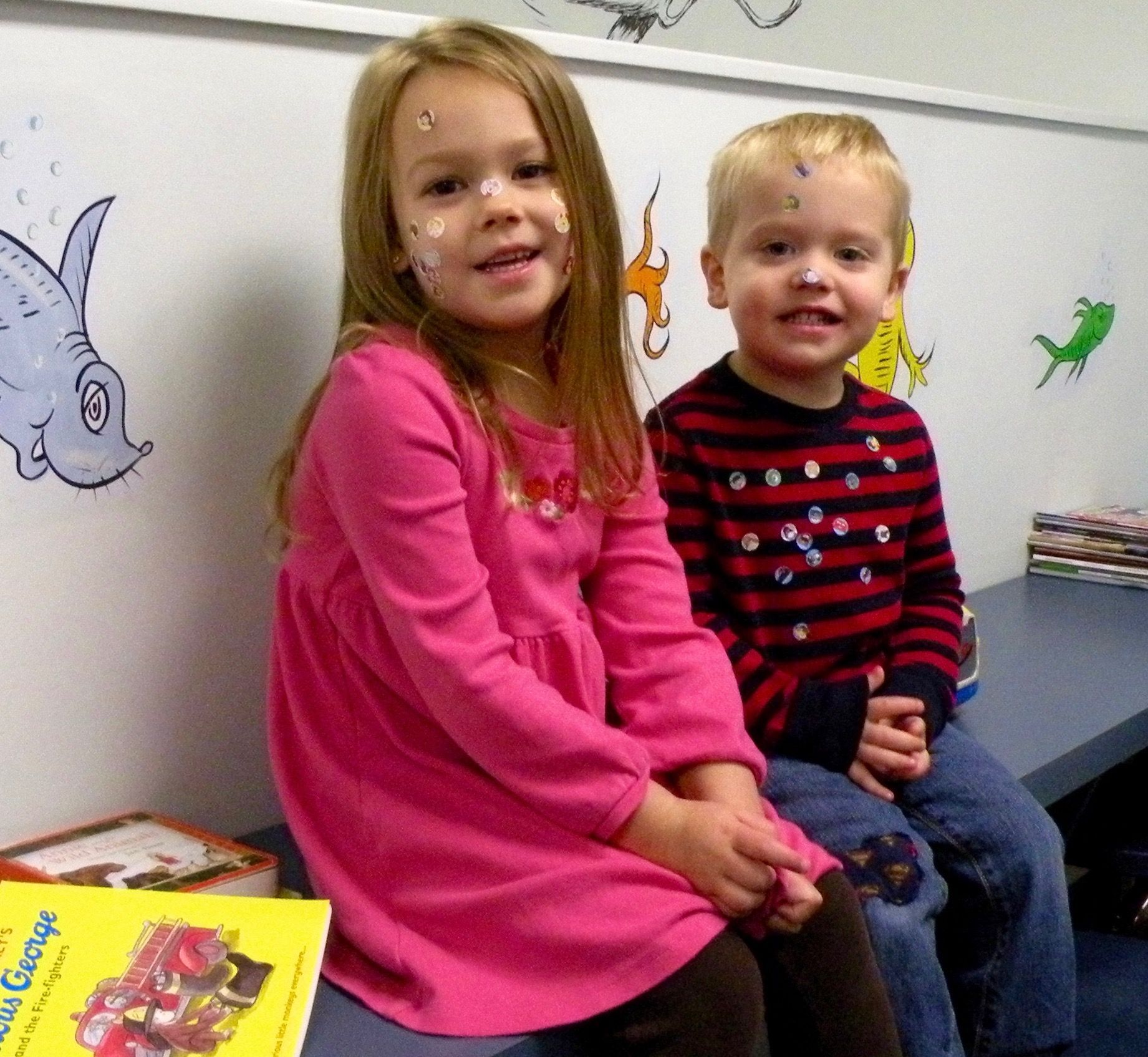 A girl in a pink dress sits next to a boy in a red and black striped shirt