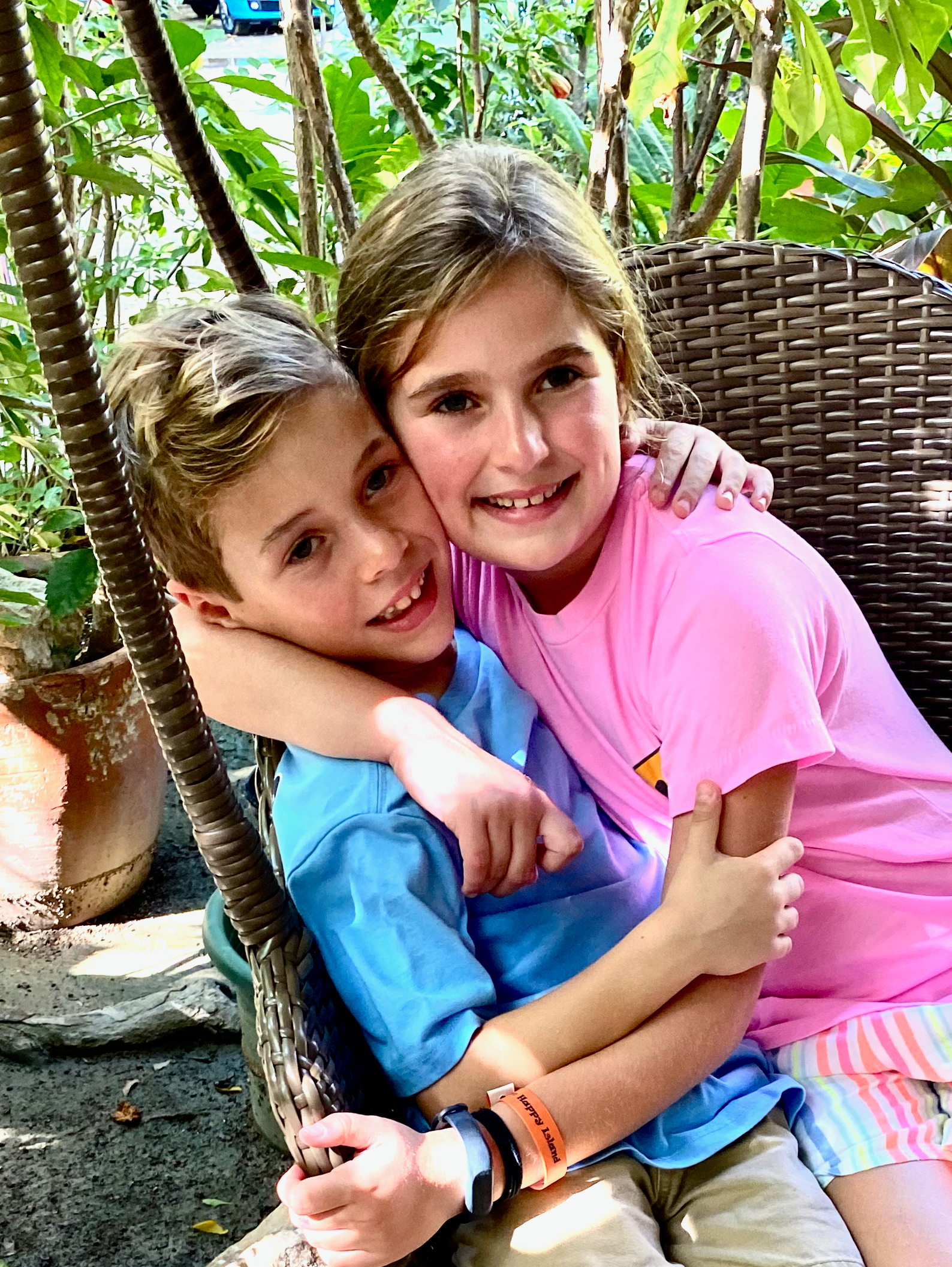 Young Boy and girl hugging with plants in the background.