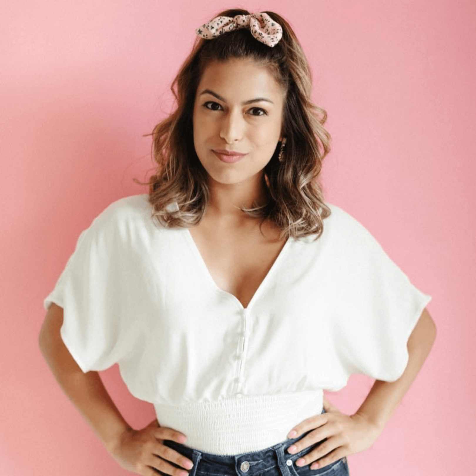 A woman wearing a white shirt and jeans is standing with her hands on her hips.