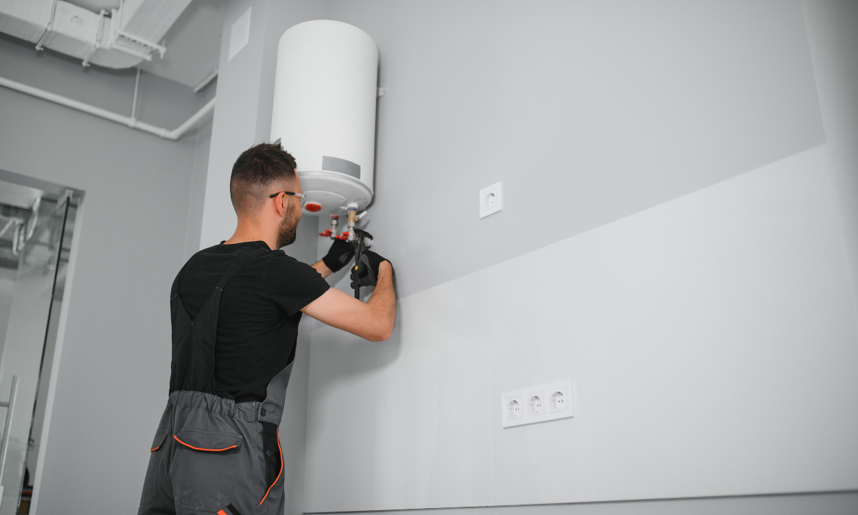 Person installing a white water heater on a gray wall with a power drill