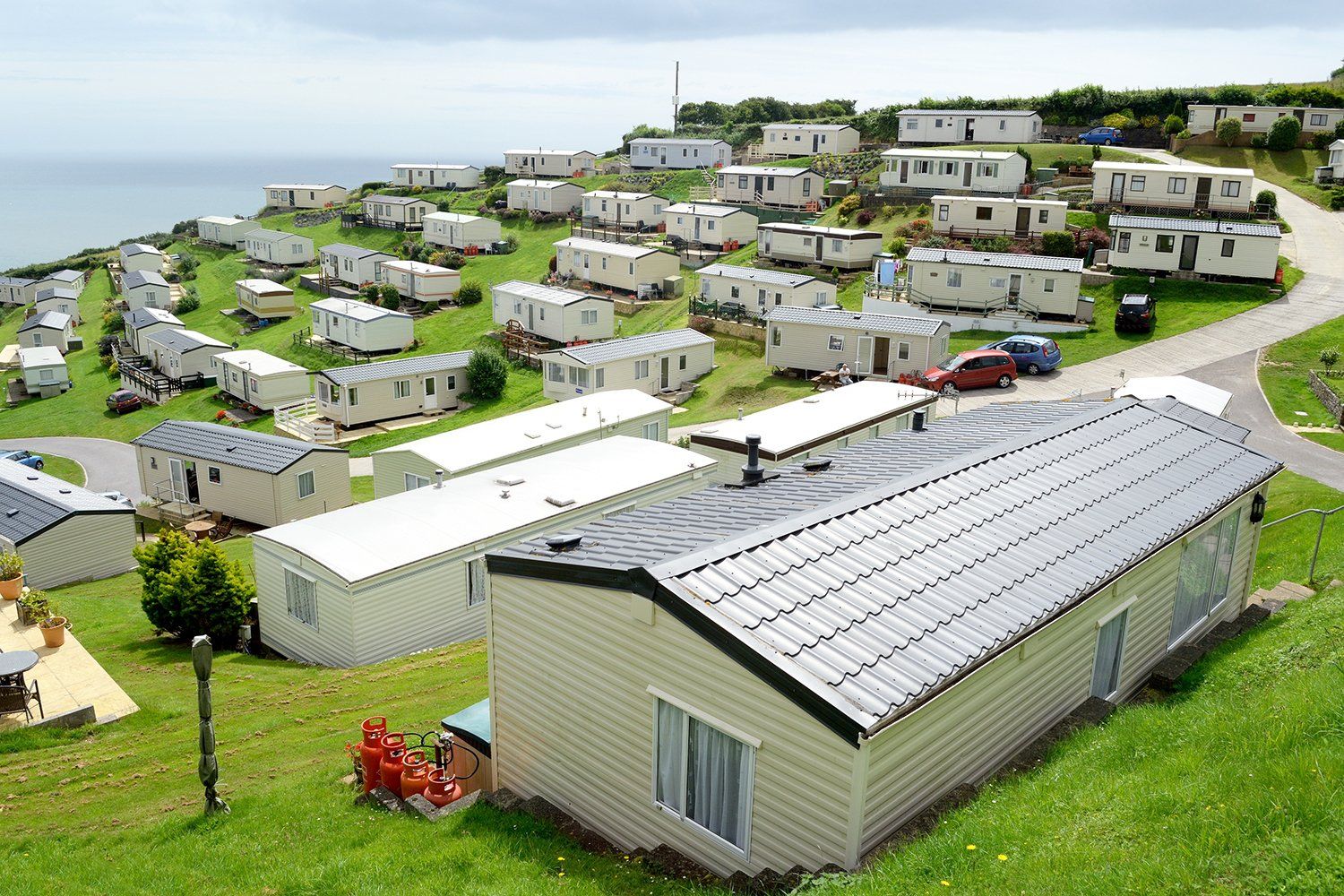 A row of mobile homes are parked in a grassy area near the ocean.
