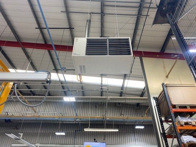 A large warm air heater is hanging from the ceiling of a warehouse.