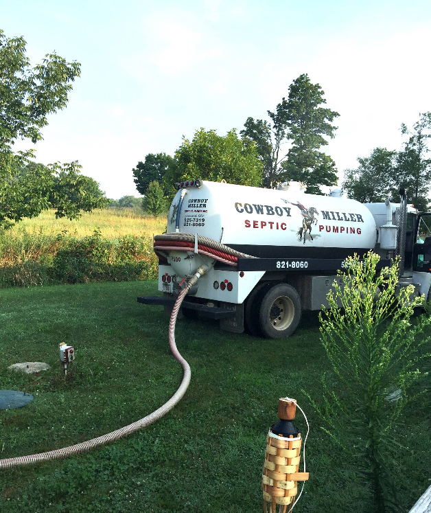 Septic service truck with hose in a grassy field near trees and a fire hydrant