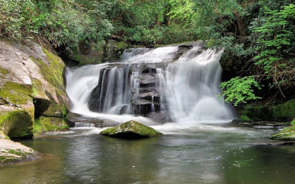 a waterfall is surrounded by trees and rocks in the middle of a river .